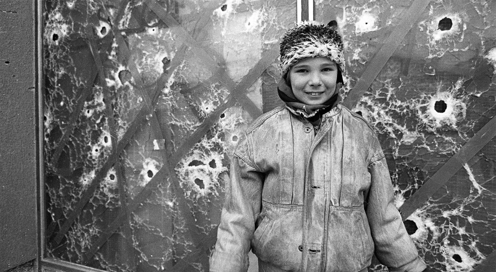 Bambina che sorride fotografata davanti a una vetrata perforata da pallottole